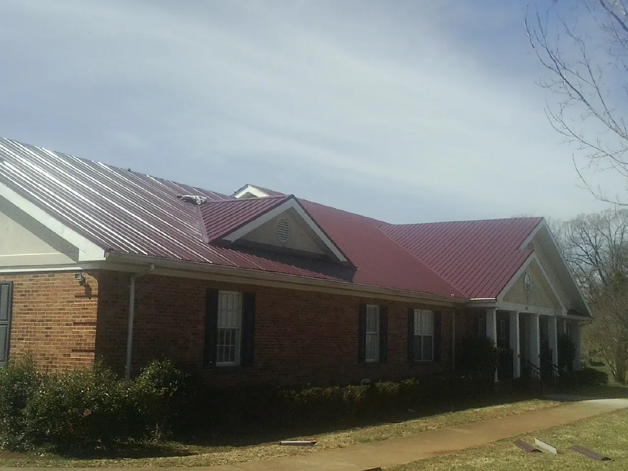 Red metal roof with gabled entries on a long brick building, from a Hail Damage Roof Repair job in Soldier