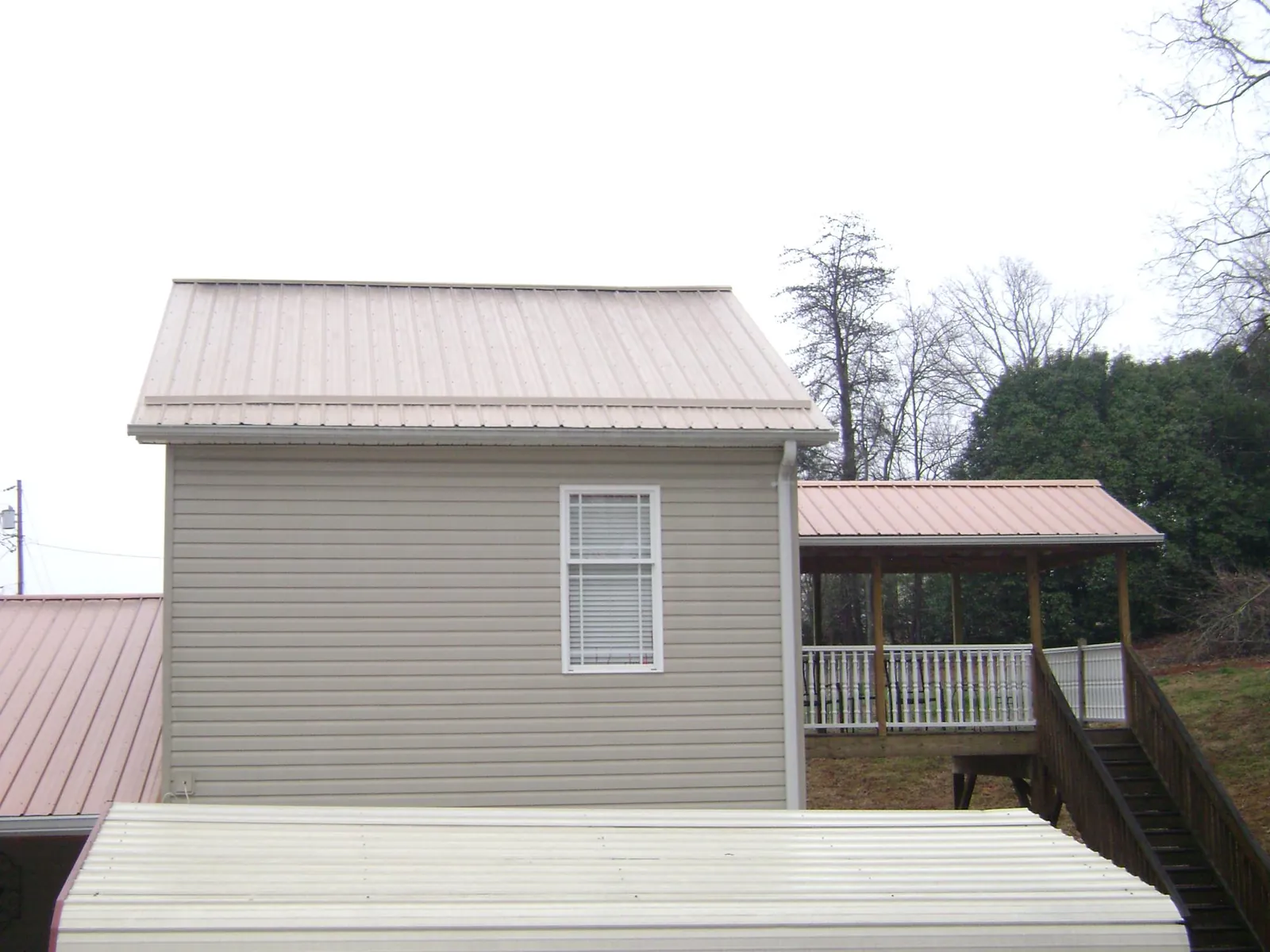 Tan metal roofs on a two story addition and attached porch, from a Roof Replacement job in Soldier